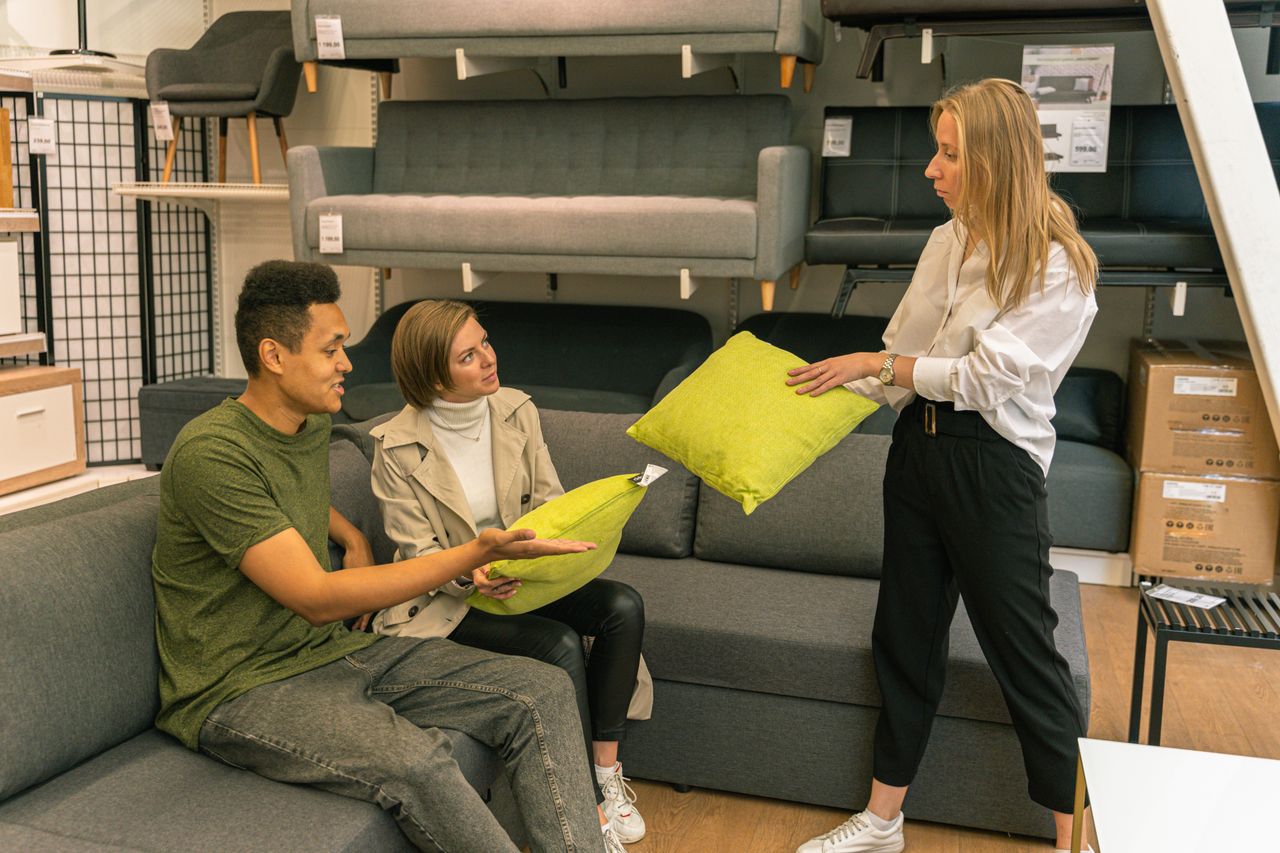Home A couple selecting cushions with a salesperson in a furniture store, surrounded by sofas.