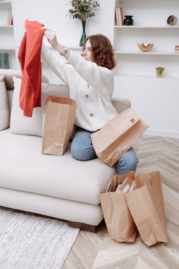 Woman sitting on a sofa unpacking shopping bags with new clothes in a stylish living room.